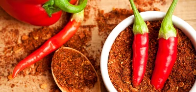 Cayenne pepper powder on a pot with some fresh and ripen peppers on a table.
